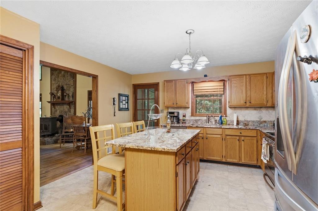 Kitchen with oak cabinets, a stone island with seating, and an open doorway to a room with a stone fireplace.