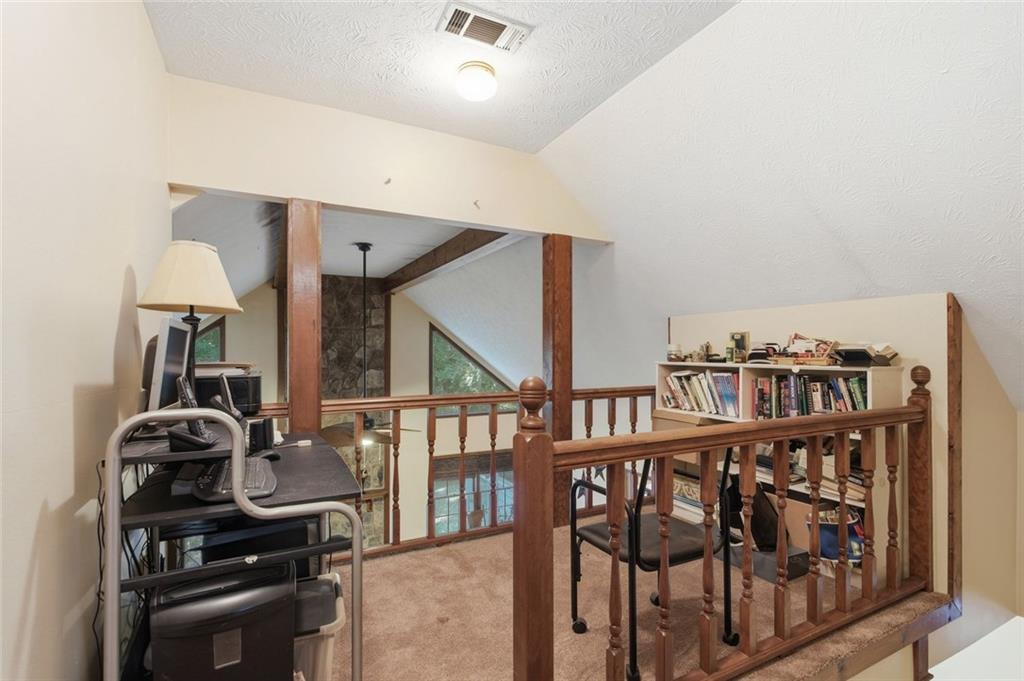 Loft landing with wooden railing, treadmill desk, bookshelves, and a high sloped ceiling.