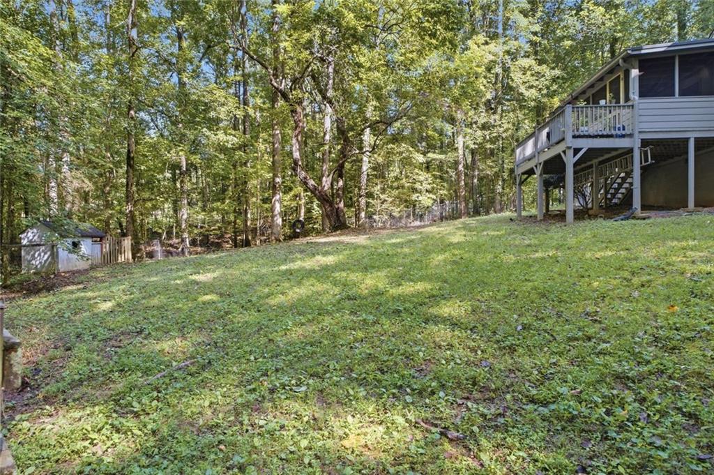 Wooded yard beside a raised house with a large deck and exterior stairs.
