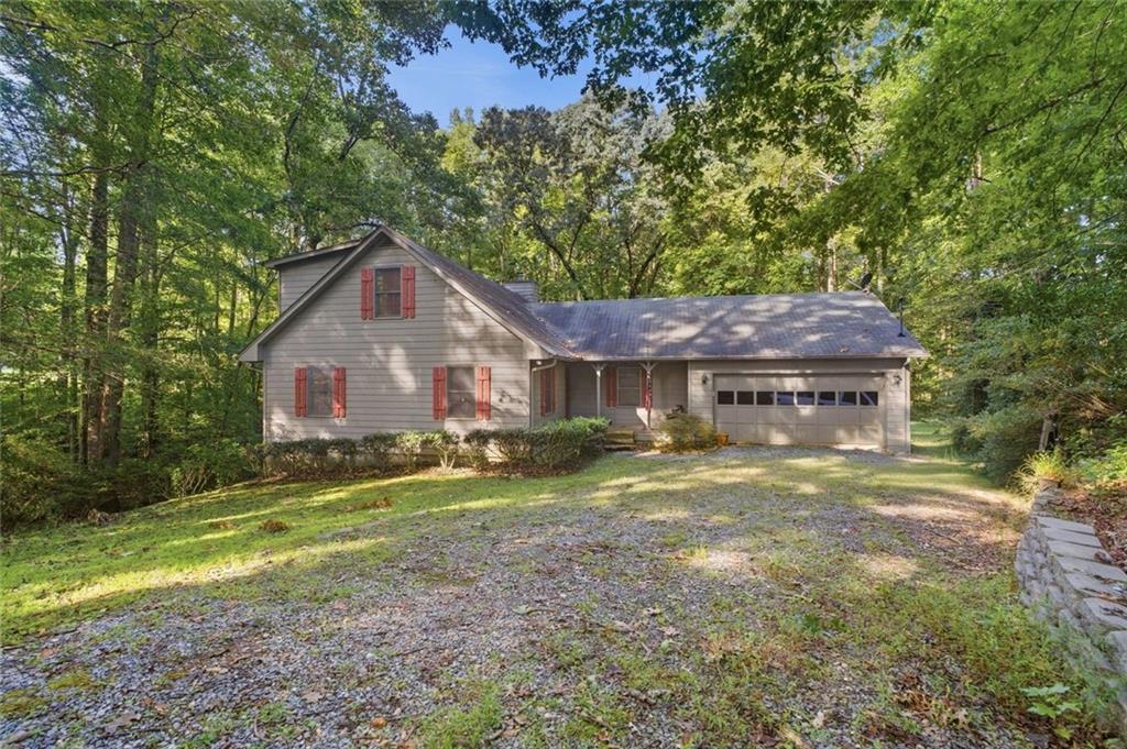 Gray gabled house with red shutters and an attached garage, surrounded by mature trees.