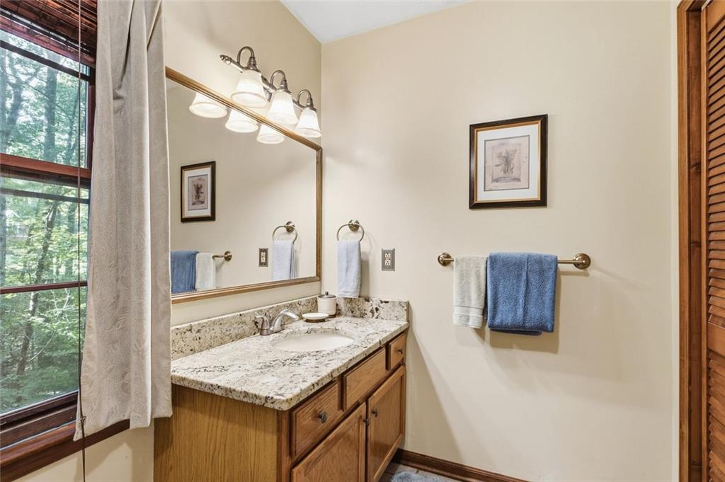 Bathroom vanity with a stone countertop, wood cabinets, and a large mirror beside a window.