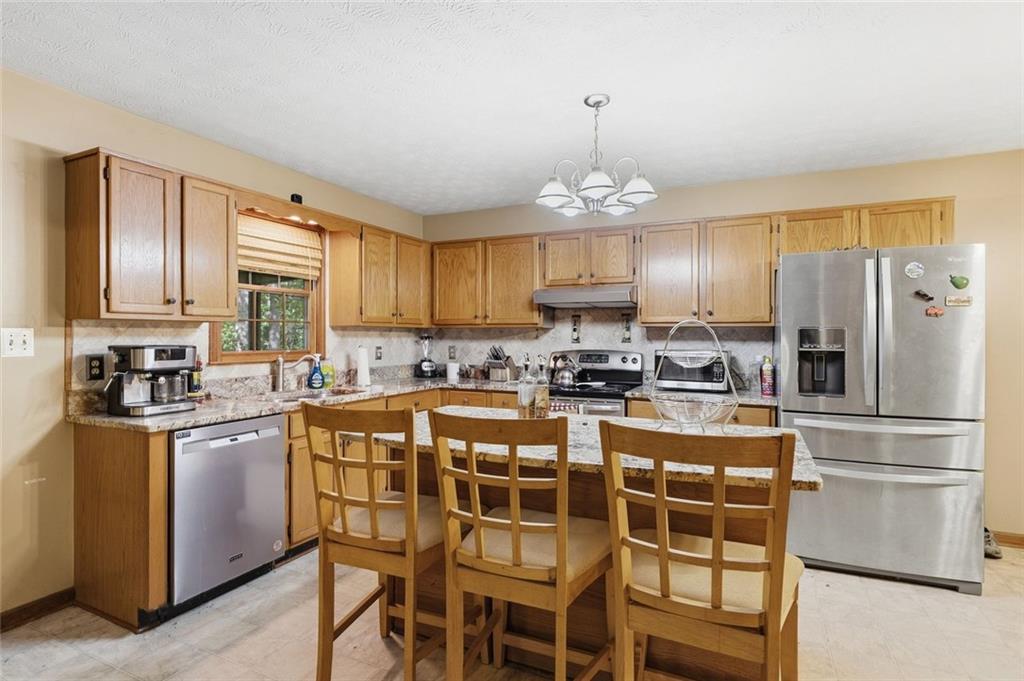 Kitchen with wood cabinets, granite counters, stainless steel appliances, and a central island with dining chairs.