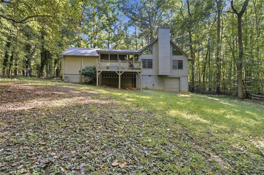 Wooded house with a raised deck, lower-level garage, and leaf-strewn lawn.