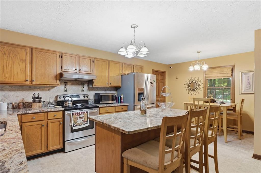 Kitchen with wood cabinets, stainless steel appliances, and a granite island with bar seating.