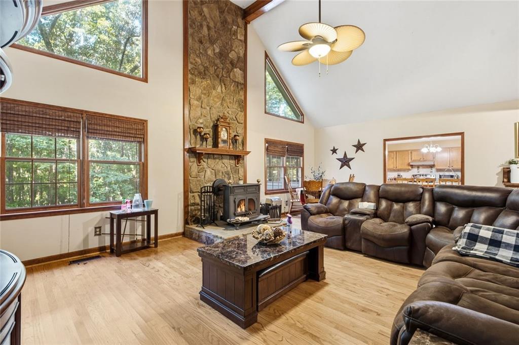 Living room with a stone fireplace, vaulted ceiling, tall windows, and brown leather sectional.