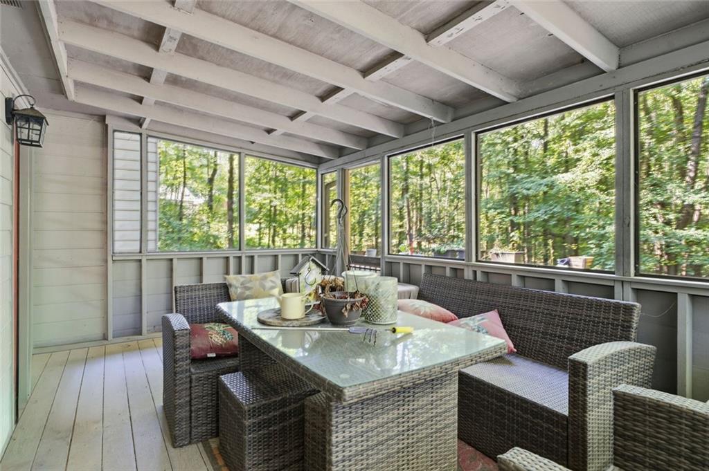 Screened-in porch with woven seating and a glass-top table overlooking leafy woods.