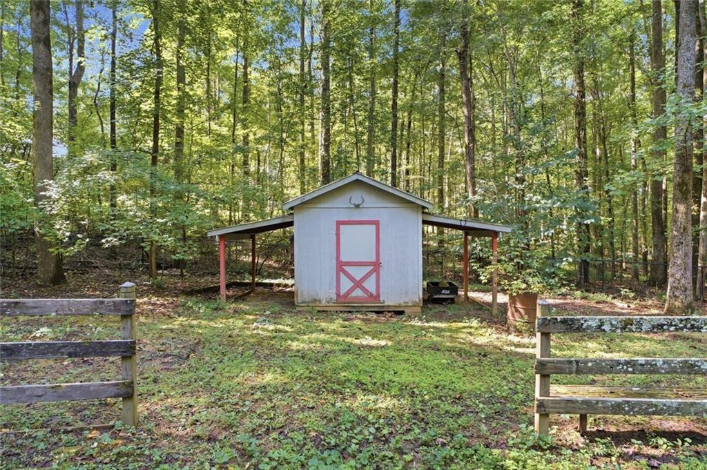 Gray shed with a red-trimmed door and open-sided lean-tos in a wooded yard.