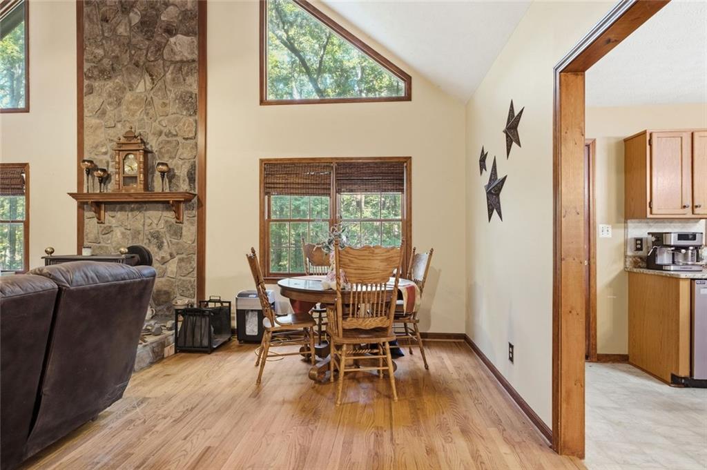 Dining area with a wooden table beside a tall stone fireplace and vaulted ceiling.