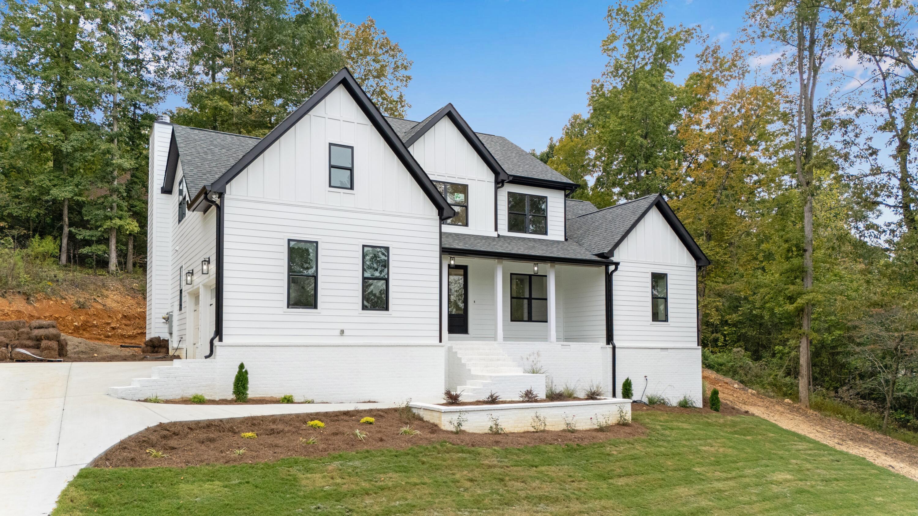 White two-story farmhouse with black trim, multiple gables, and a covered front porch among trees.