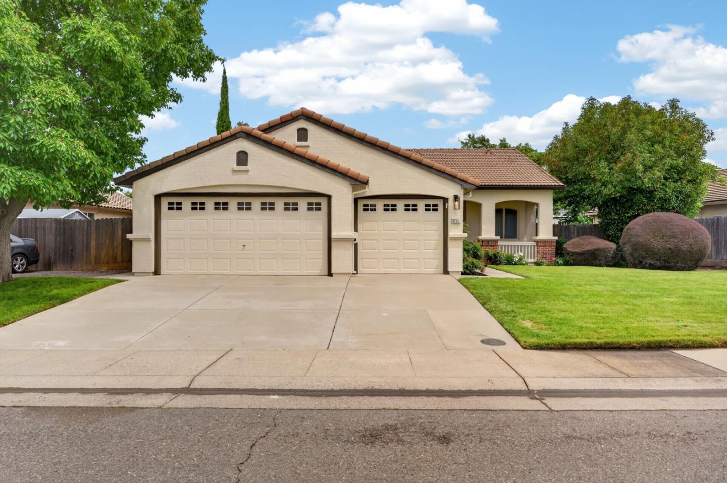 Beige stucco home with two garage doors, a tiled roof, wide driveway, and landscaped front lawn.