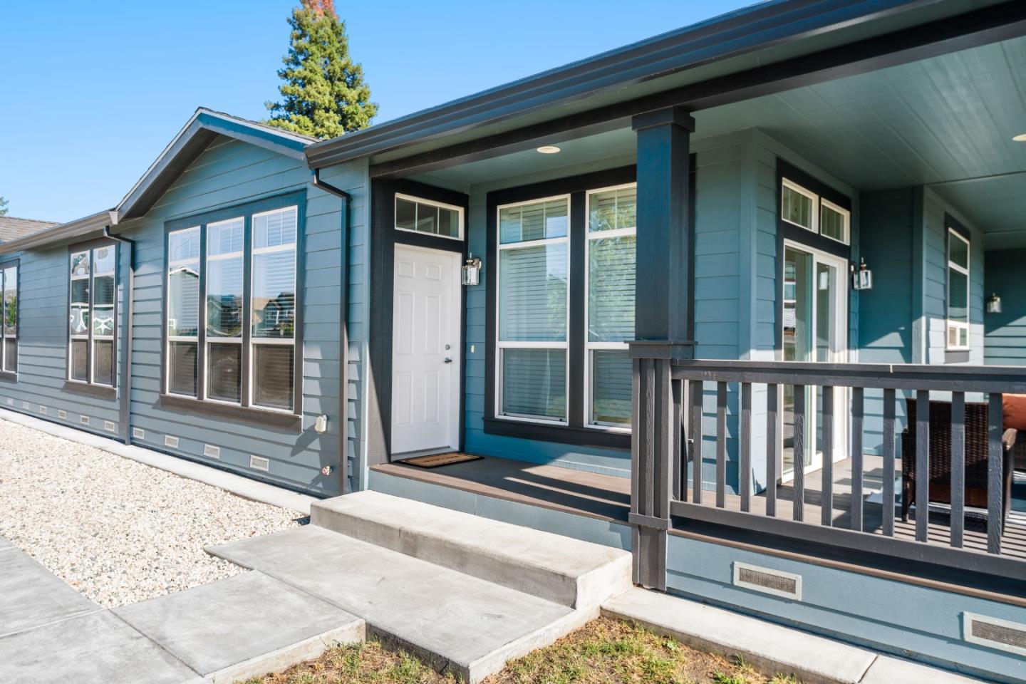 Blue-gray home with a covered porch, dark railing, and gravel landscaping.