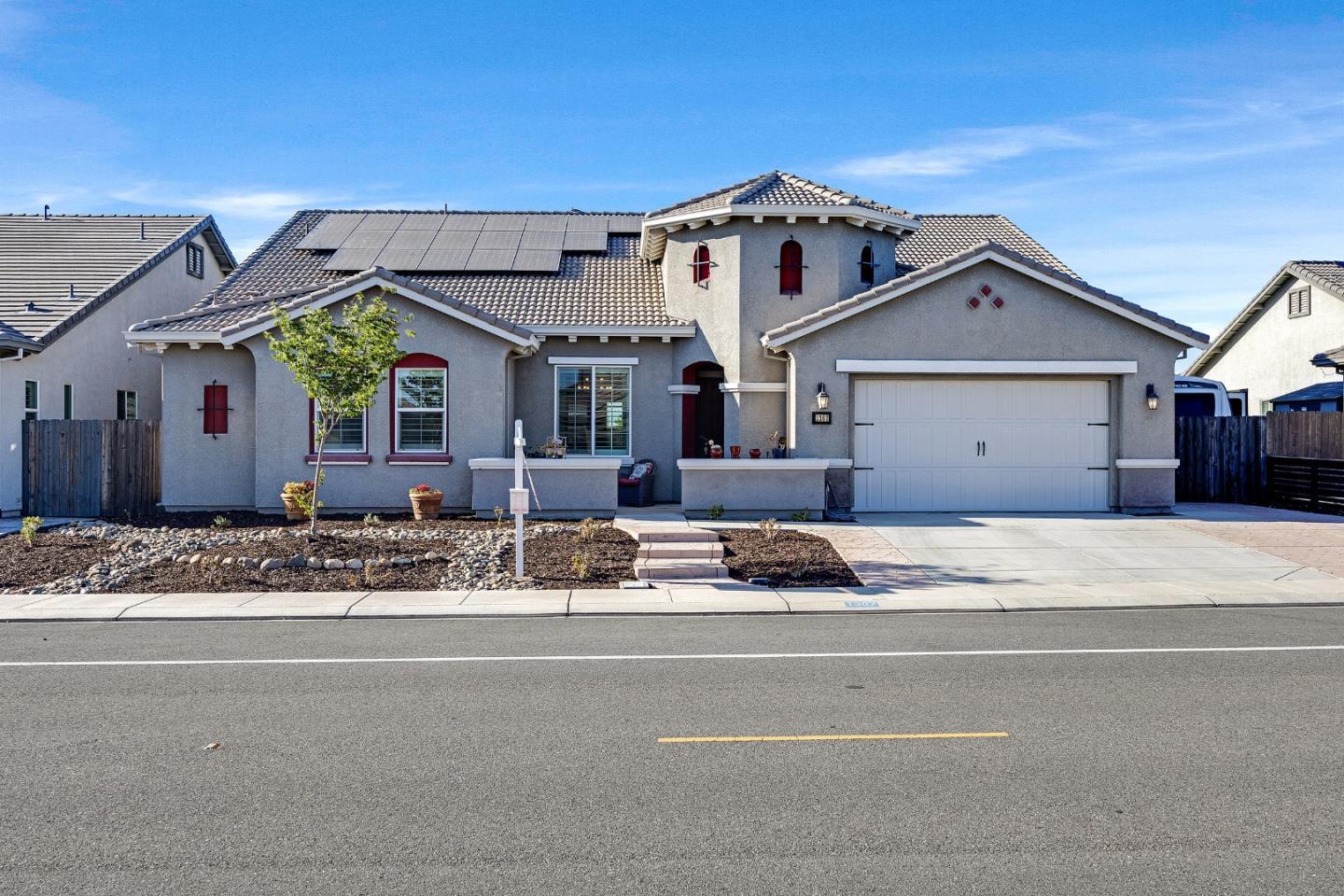 Gray stucco house with rooftop solar panels, tiled roof, and attached two-car garage.