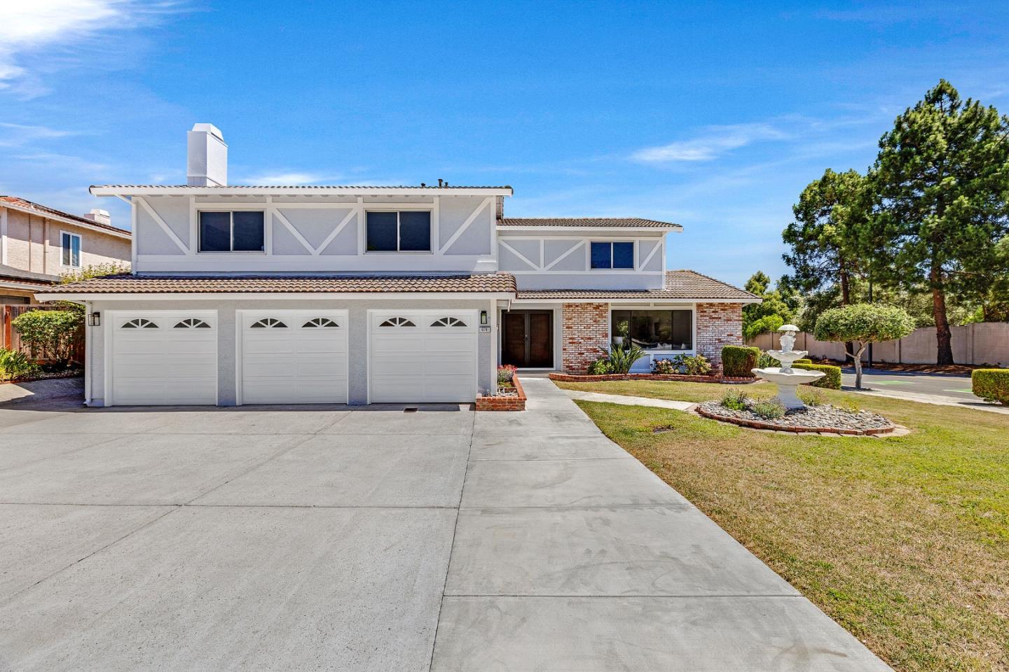 Two-story white house with three garage doors, brick accents, and a landscaped yard with a fountain.
