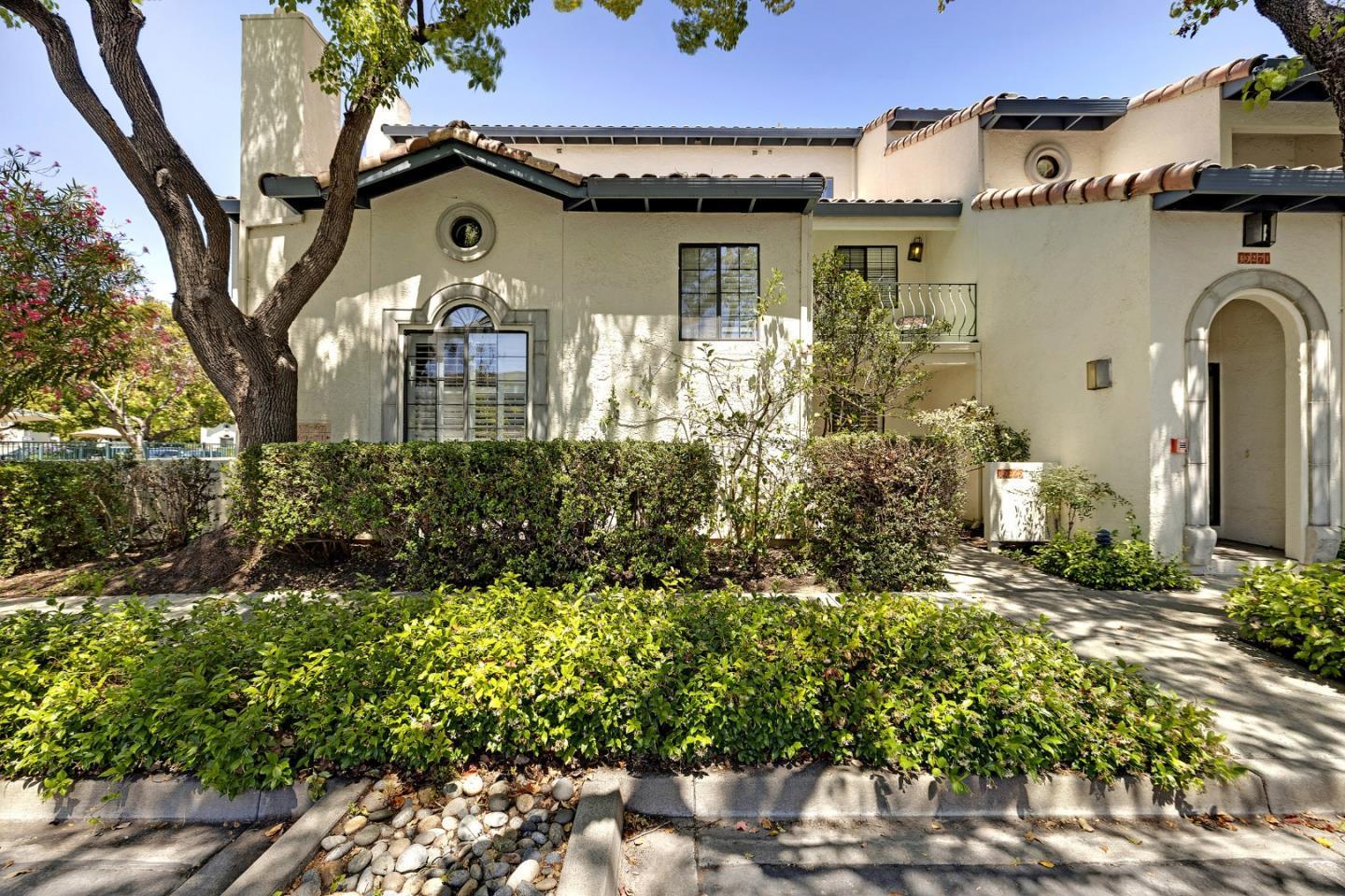 Cream stucco residence with a tiled roof, arched entry, circular windows, and landscaped frontage.