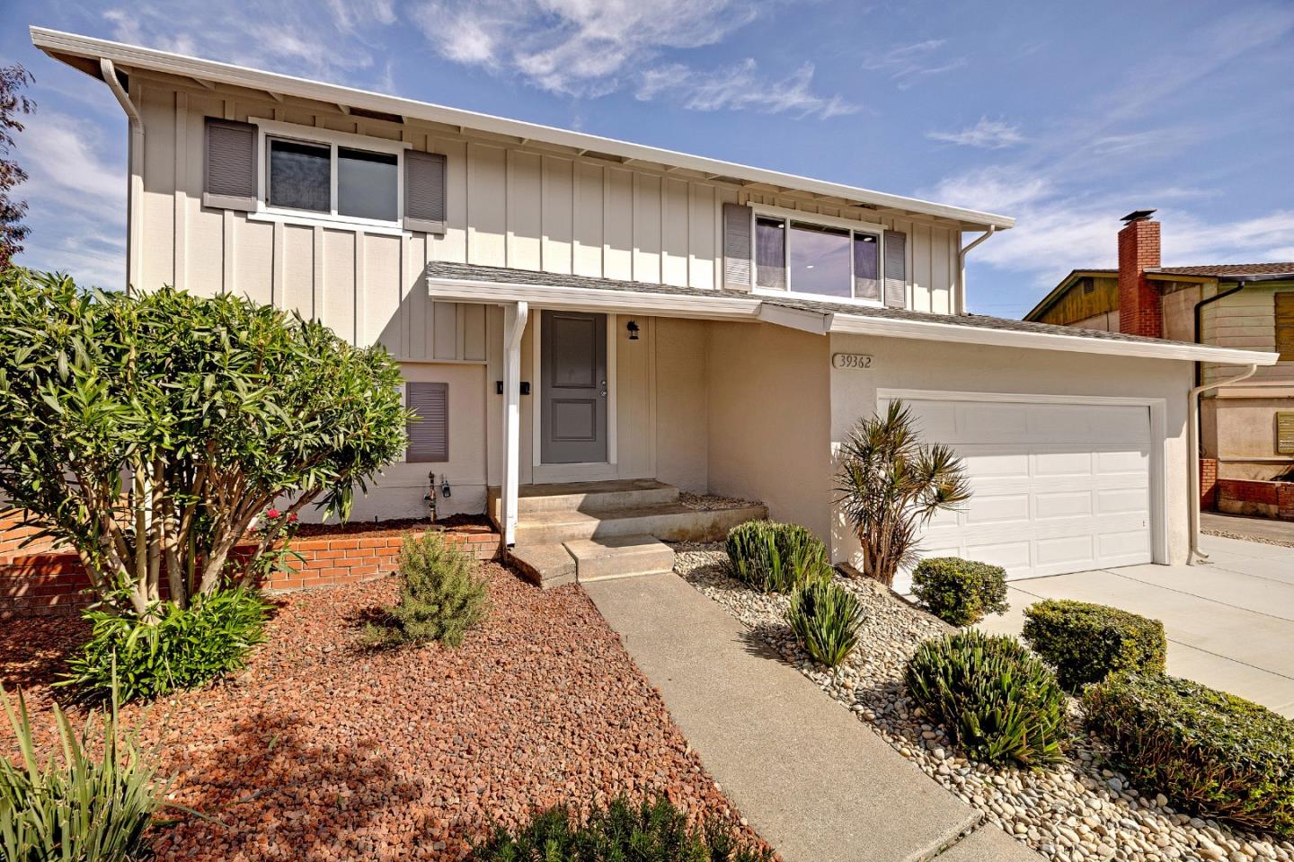 Two-story beige home with a gray entry door, double garage, and rock landscaping.