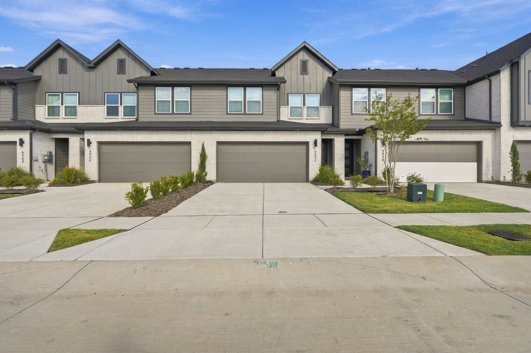 Attached gray two-story townhomes with brick façades, garage doors, and landscaped driveways.