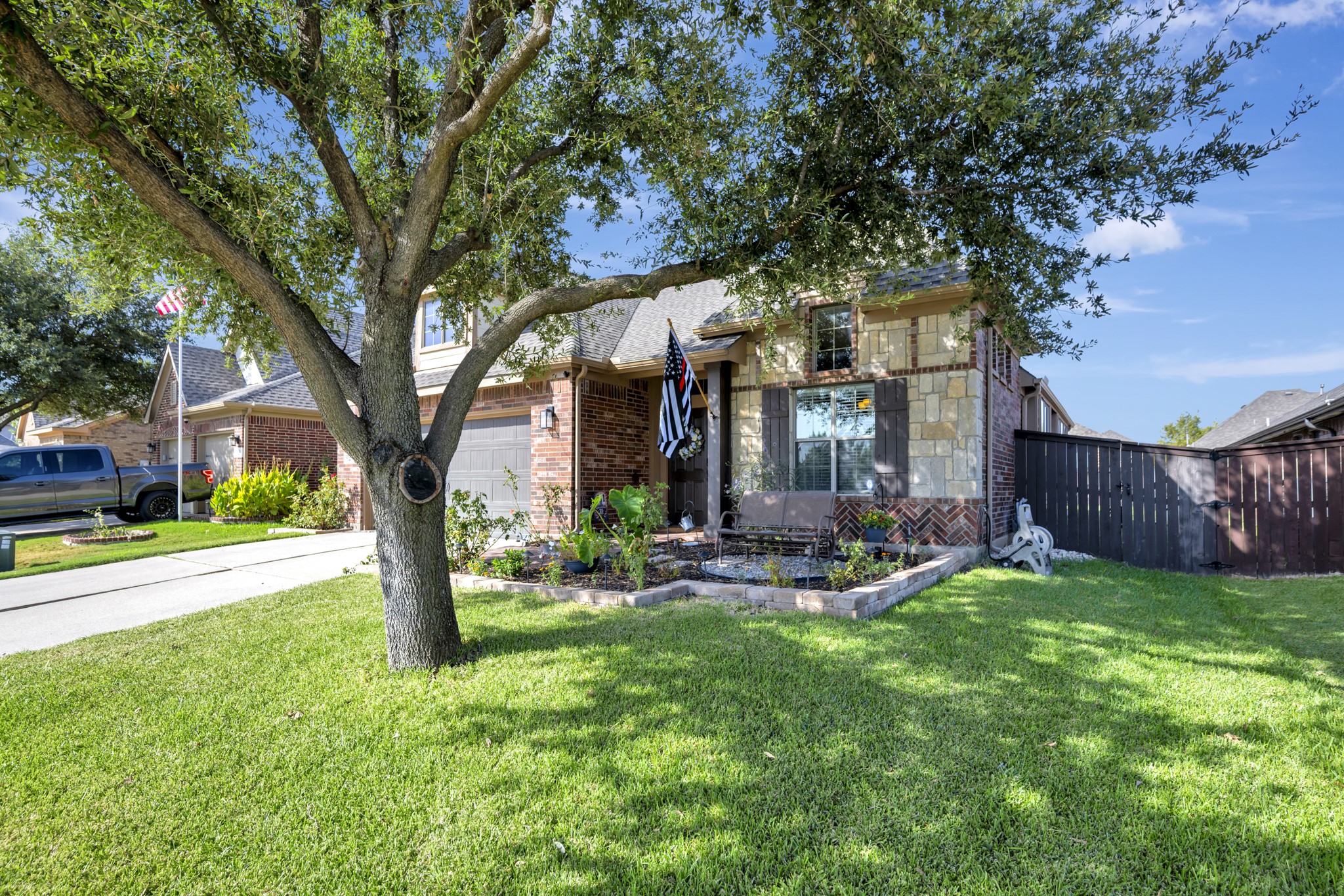 Brick and stone home behind a mature shade tree, landscaped garden, and broad green lawn.