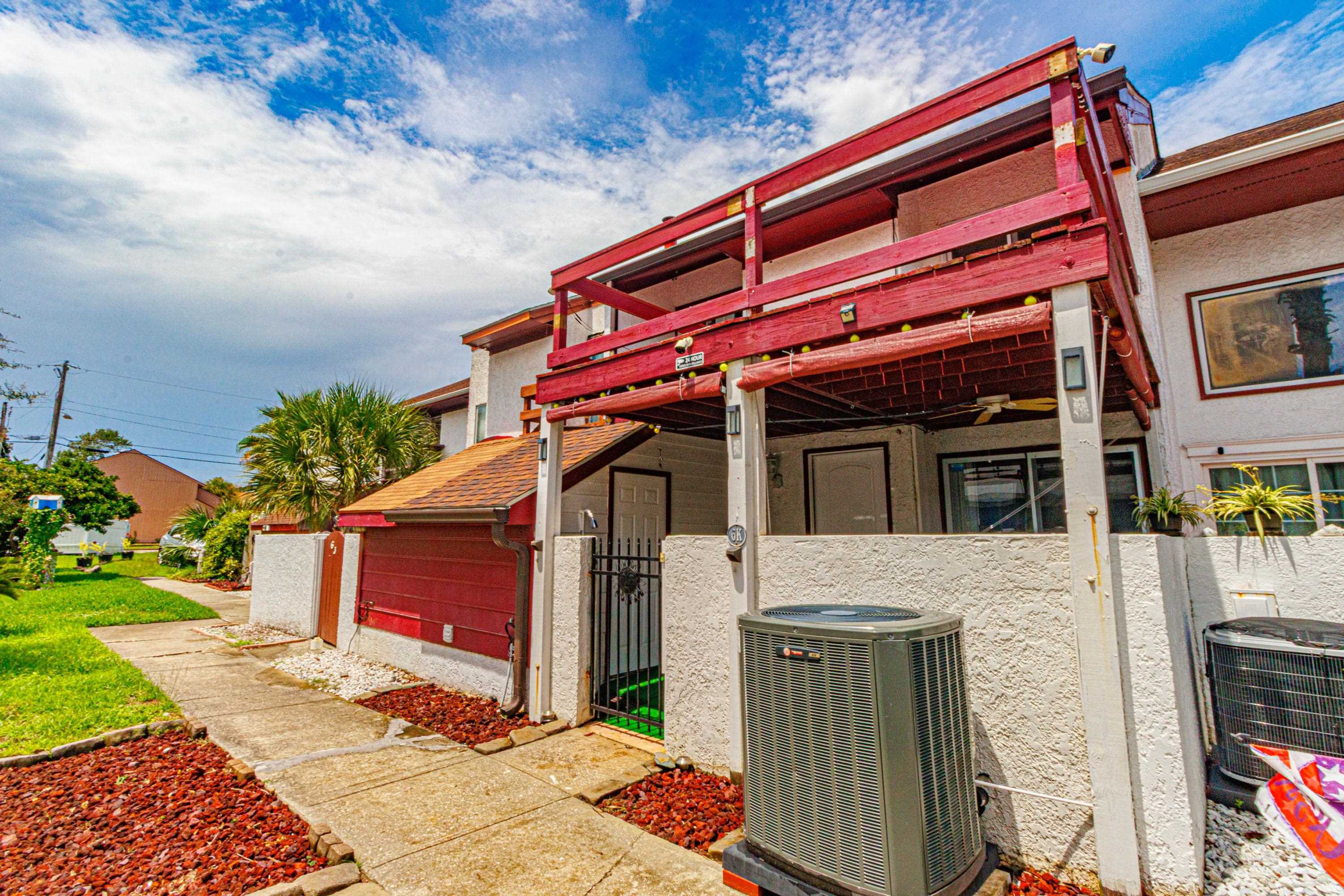 Townhouse exterior with a raised red deck, gated patio entrance, and landscaped walkway.