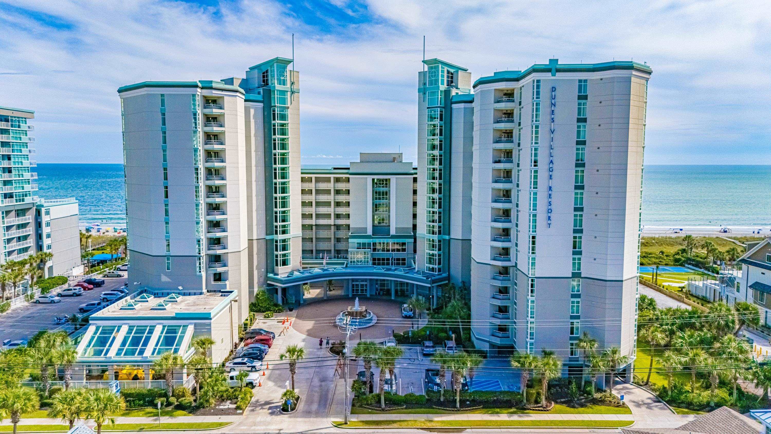 Dunes Village Resort towers beside the ocean, viewed from above with the beach in the background.