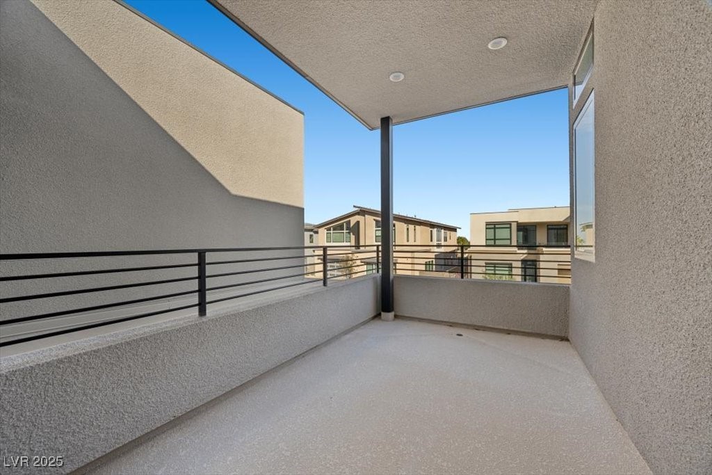 Covered balcony with black railing overlooking neighboring modern homes.