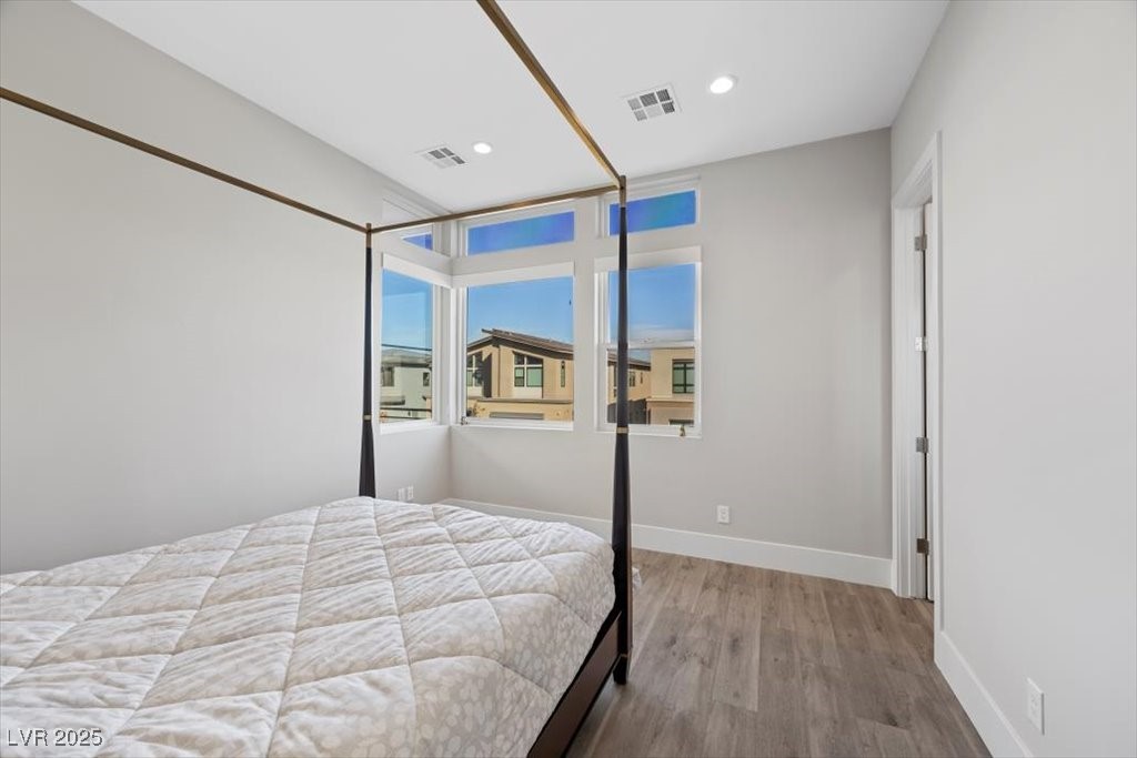 Bedroom with a four-poster bed, gray wood-look flooring, and tall windows overlooking neighboring homes.