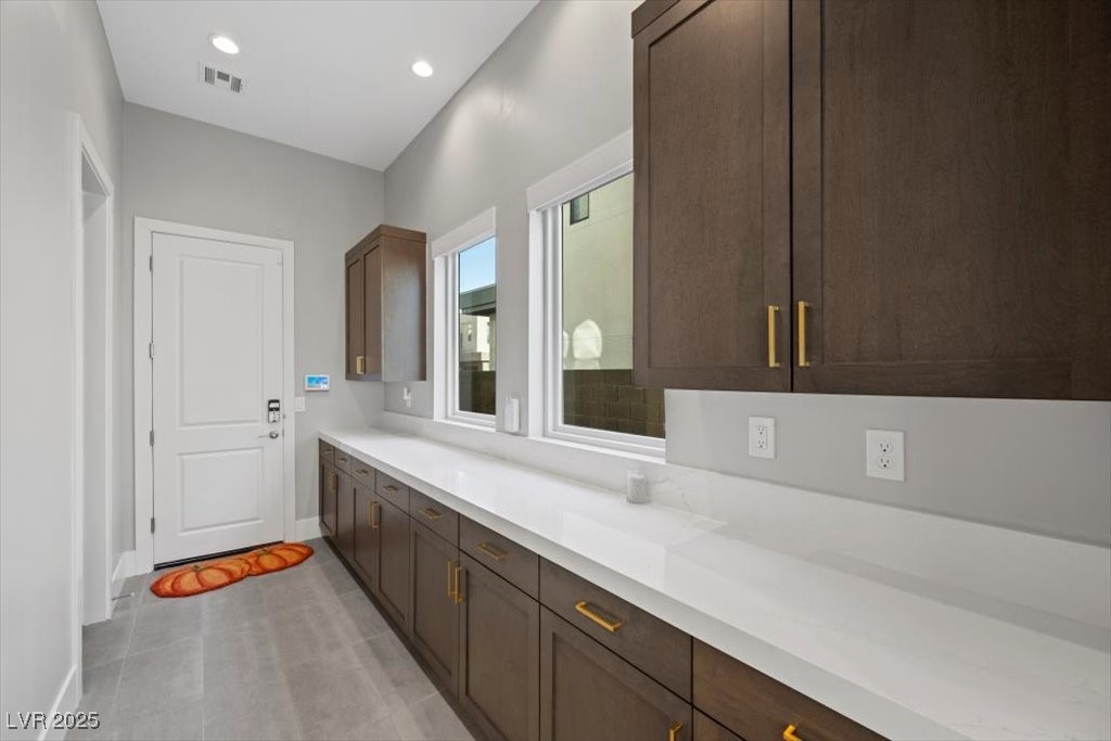 Laundry room with a long white counter, dark wood cabinets, and two windows.