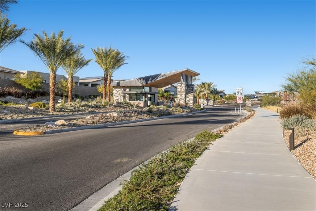 Gated community entrance with a modern guardhouse, palm trees, and desert landscaping.
