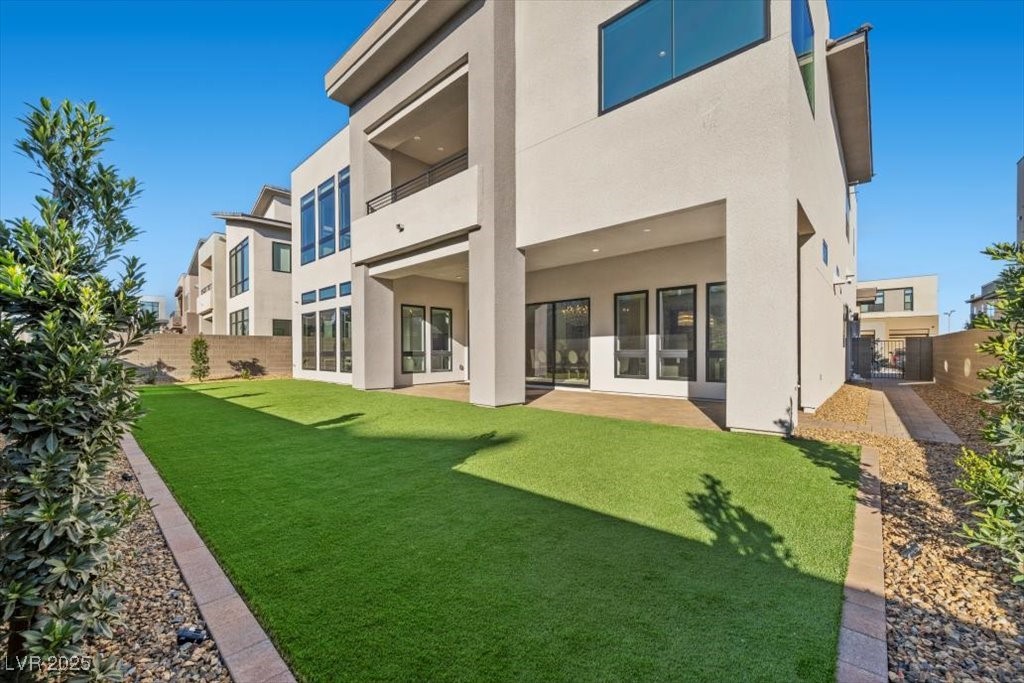 Modern home’s rear exterior with a covered patio and broad green lawn.
