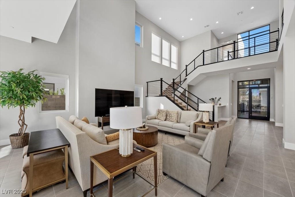 Double-height living room with neutral sofas, gray tile flooring, and a black metal staircase.