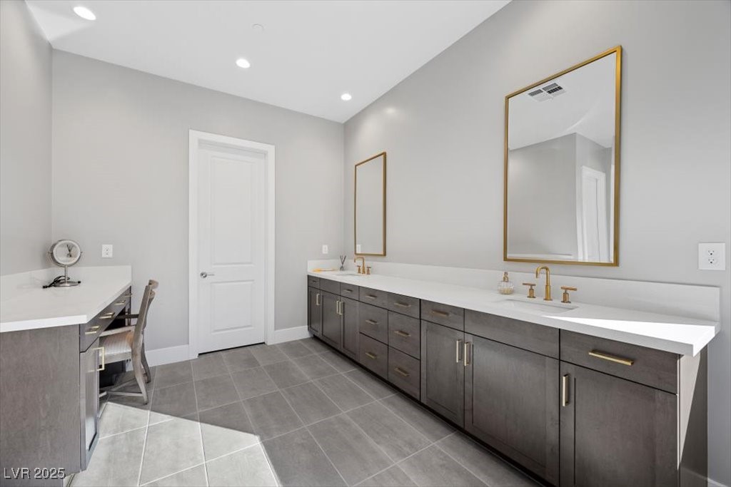 Bathroom with a long double vanity, gray cabinets, gold fixtures, and a makeup desk.