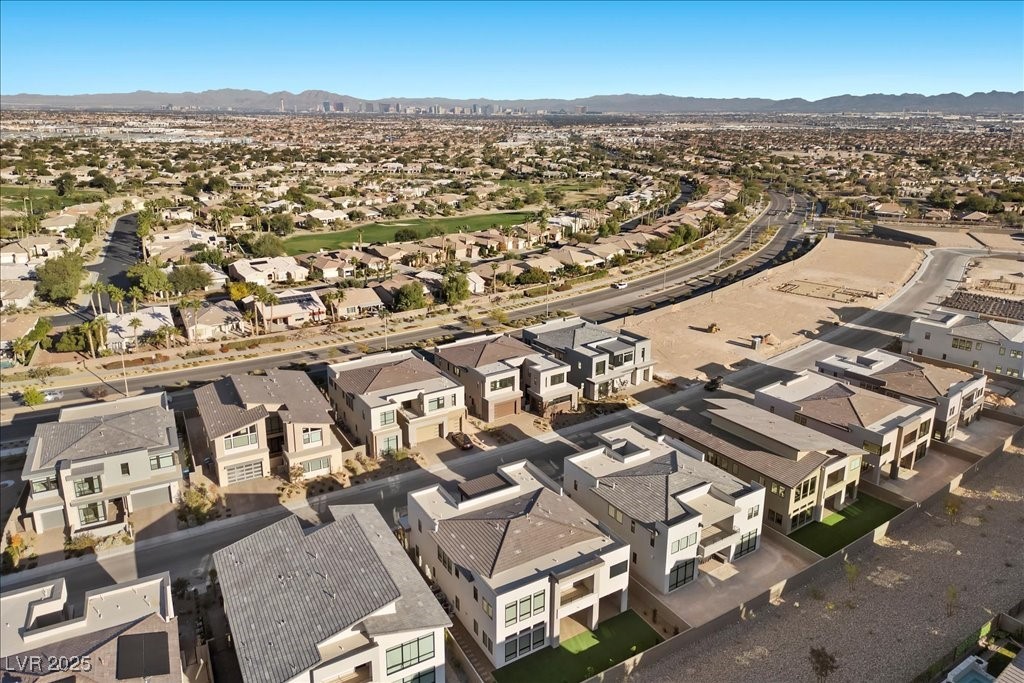 Aerial view of modern homes and open lots, with the Las Vegas skyline and mountains beyond.