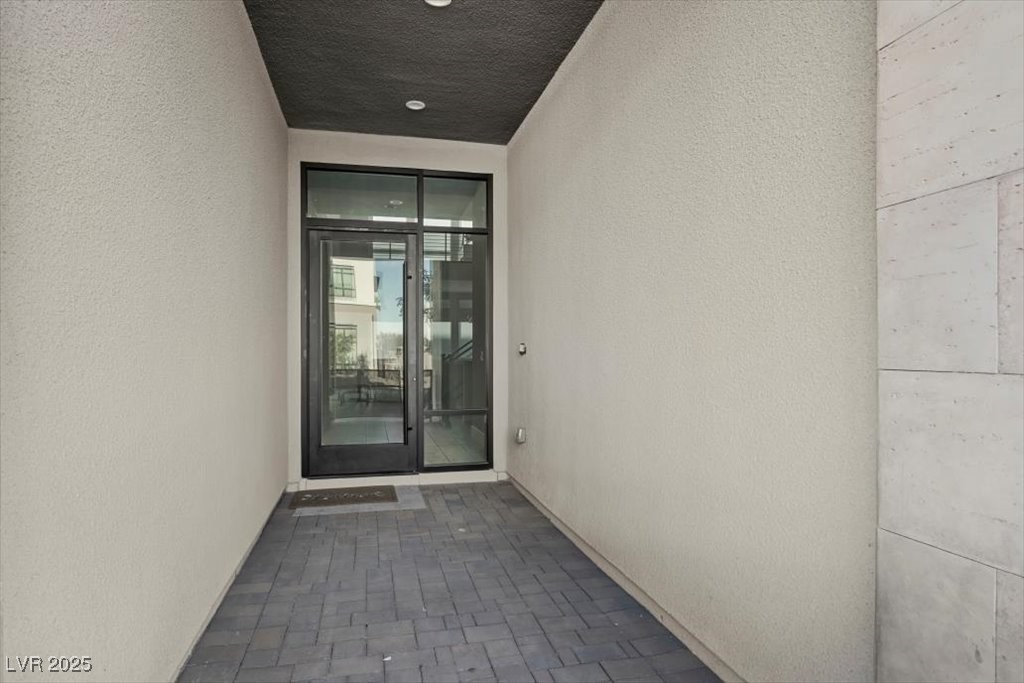 Covered home entrance with gray pavers and a black-framed glass door.