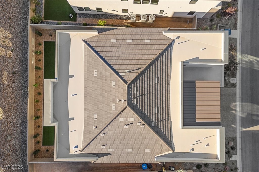 Aerial view of a home with intersecting gray shingle roofs and surrounding flat roof sections.