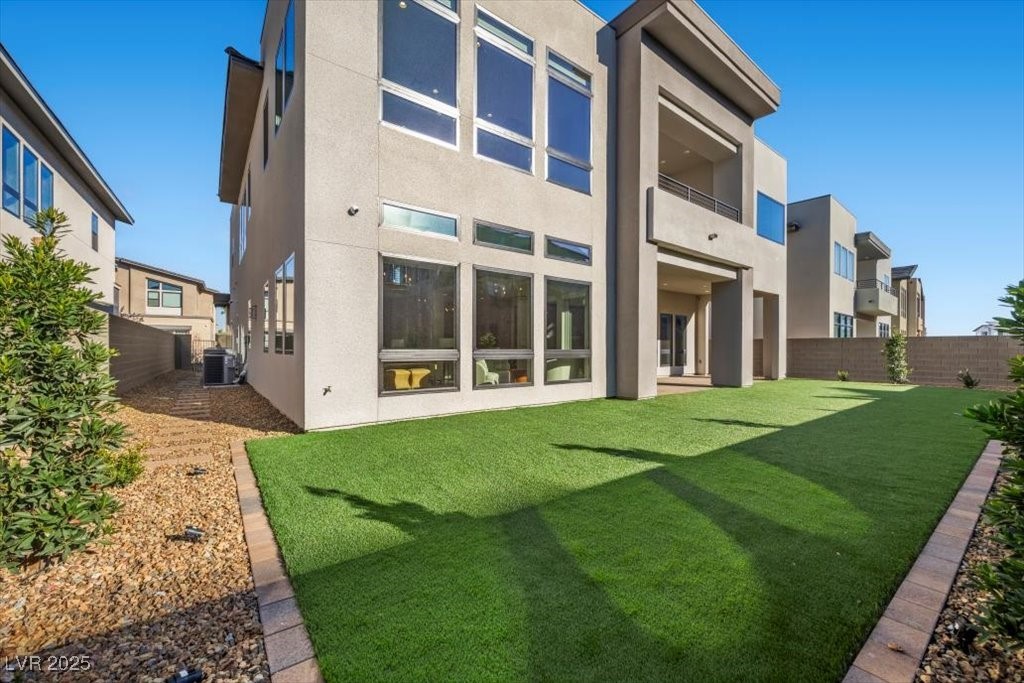 Modern home’s rear exterior with large windows, covered balconies, and a broad artificial-turf yard.