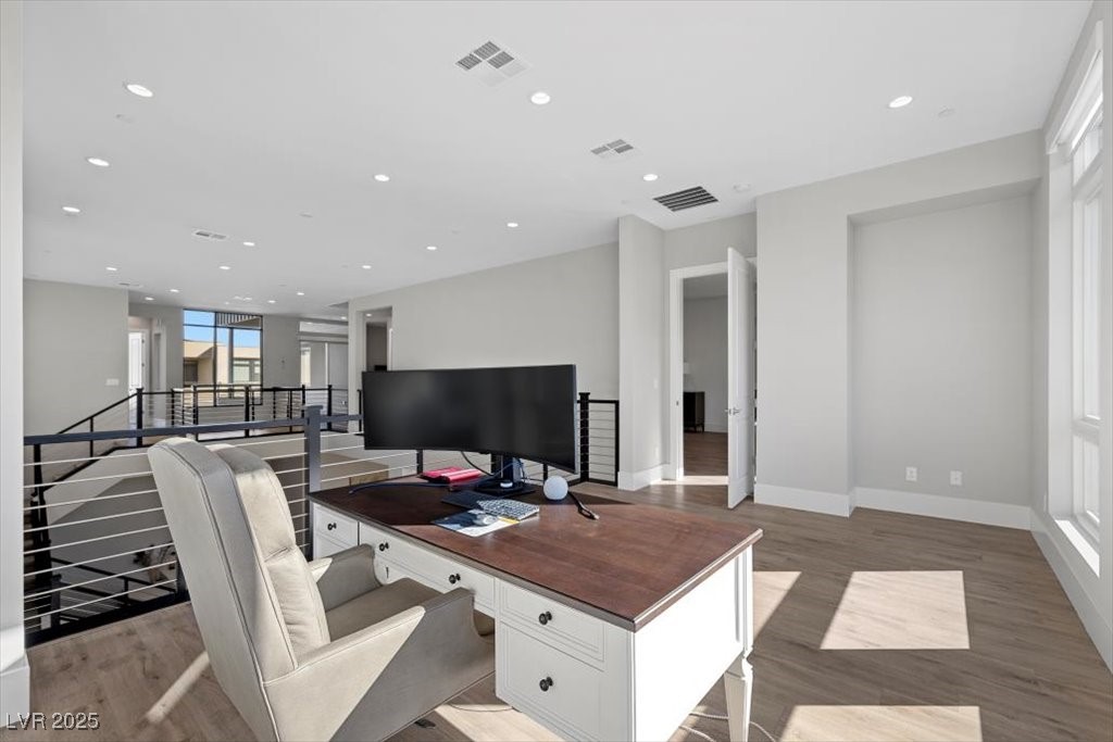 Upstairs home office with a white desk, large monitor, upholstered chair, and open stairwell.