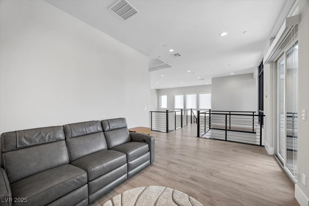 Living room with a gray sectional, wood-look floors, and black railings around an open stairwell.