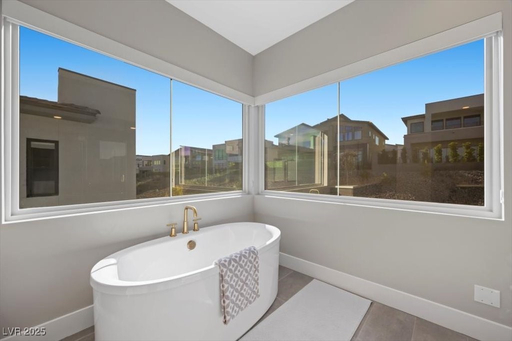 Bathroom with a freestanding tub beneath large corner windows overlooking neighboring homes.