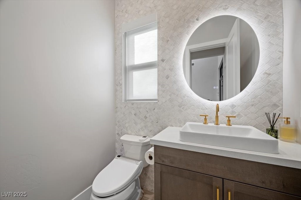 Bathroom vanity with a vessel sink, gold fixtures, round backlit mirror, and patterned tile.