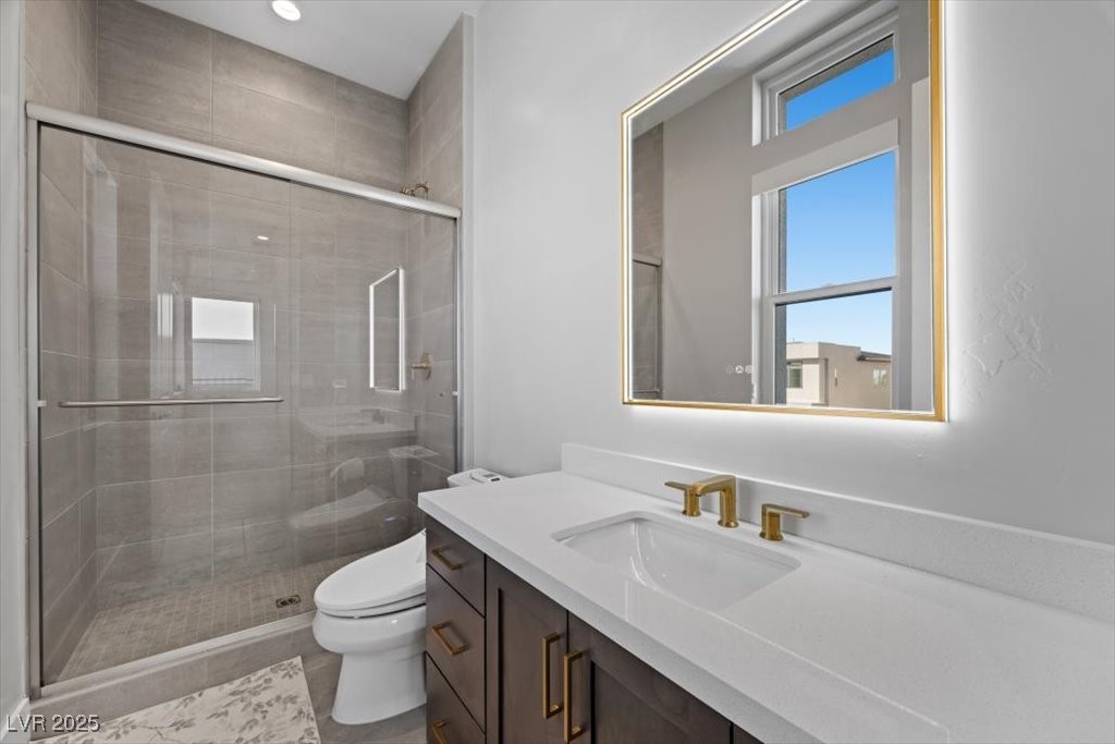 Modern bathroom with a glass-enclosed gray-tile shower, white vanity, and gold-tone fixtures.