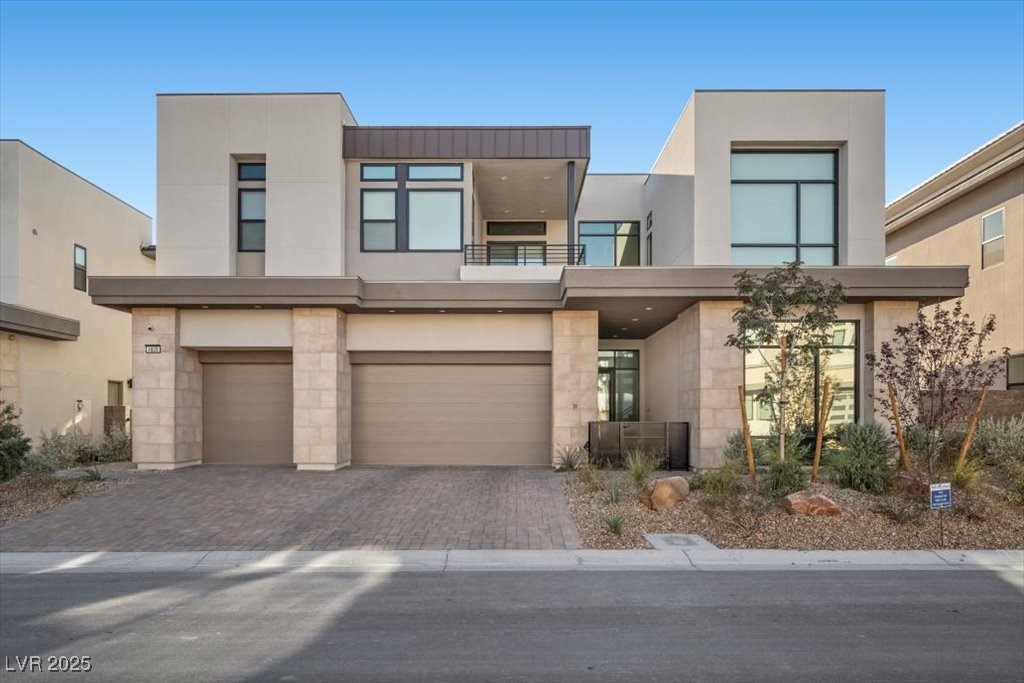 Modern two-story home with large windows, a paved driveway, and desert landscaping.