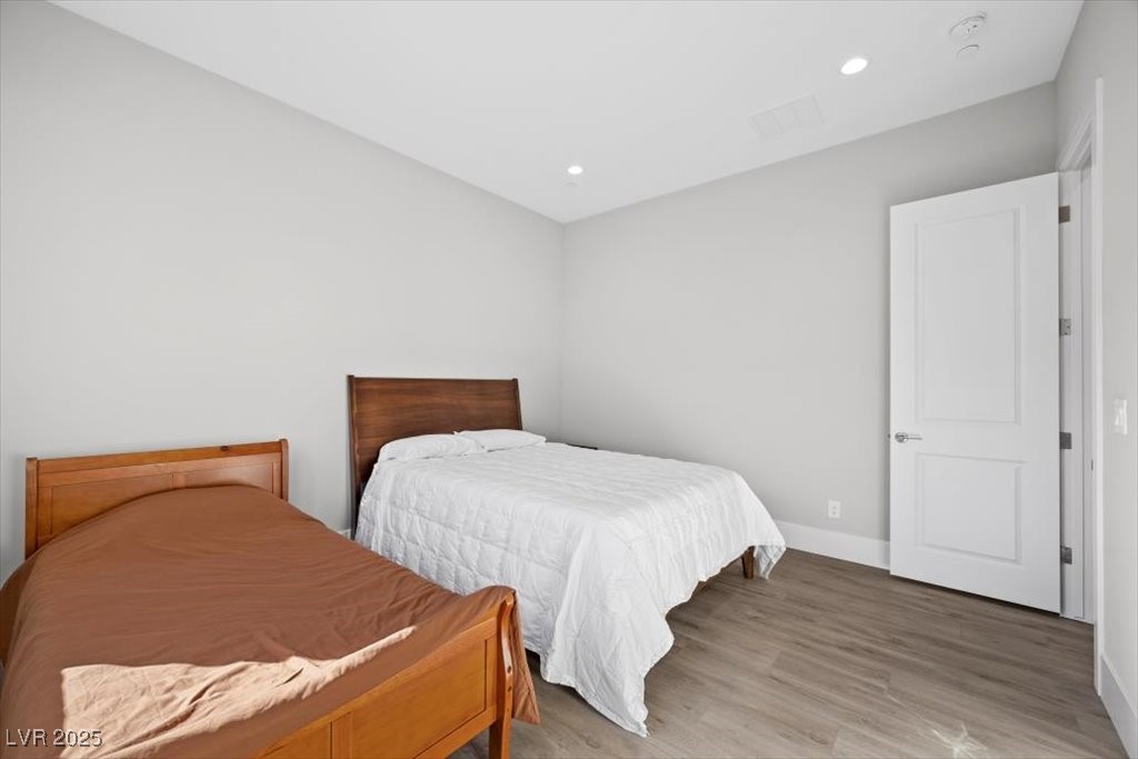 Bedroom with two beds, gray wood-look flooring, and an open white door.