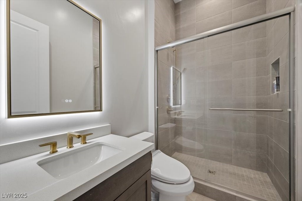 Modern bathroom with a gold-tone faucet, illuminated mirror, and glass-enclosed gray-tile shower.