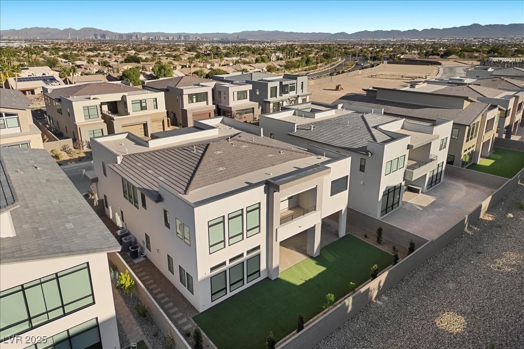 Aerial view of modern homes with artificial-turf yards, desert mountains, and the distant Las Vegas skyline.