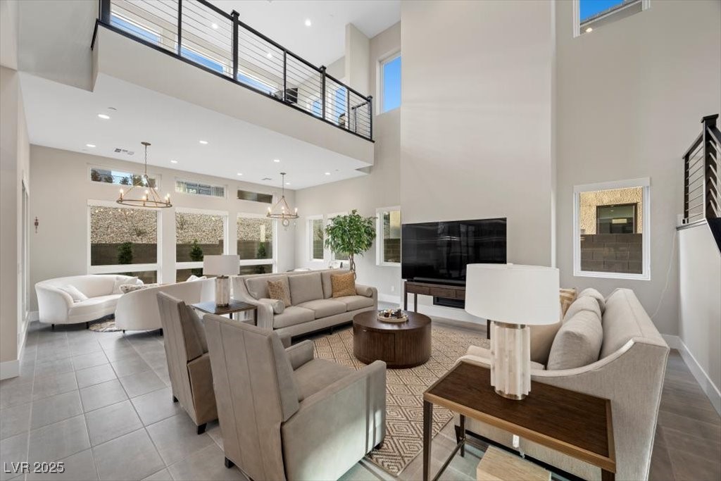 Staged living room with soaring ceilings, an upstairs walkway, large windows, and neutral seating.