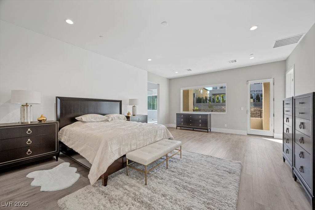 Spacious staged bedroom with a large bed, dark wood dressers, and glass doors to a courtyard.