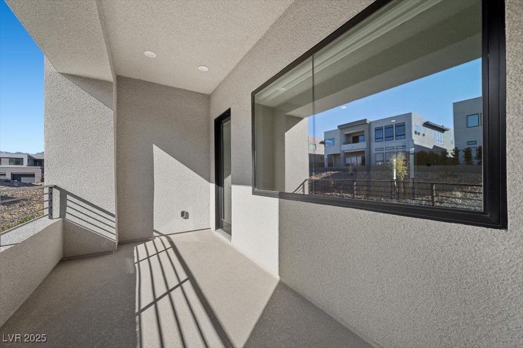 Covered balcony with a metal railing and large window reflecting neighboring modern homes.