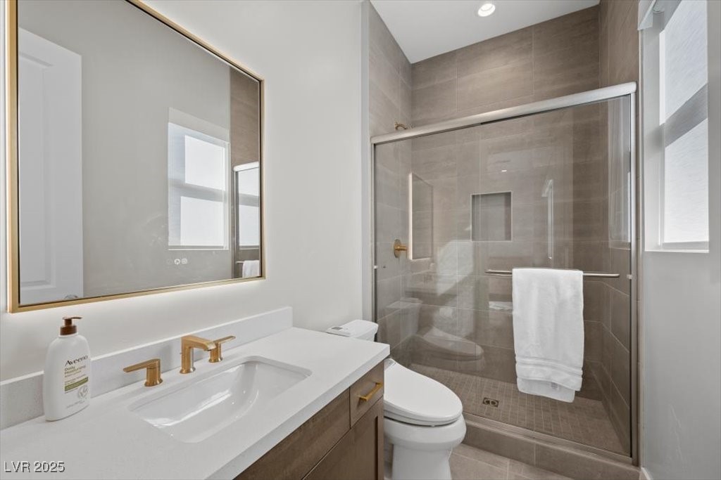 Modern bathroom with a white vanity, gold fixtures, and a glass-enclosed gray-tile shower.