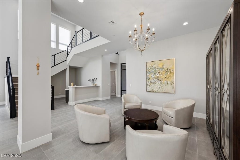 Furnished sitting area with cream chairs, a dark round table, chandelier, and staircase.