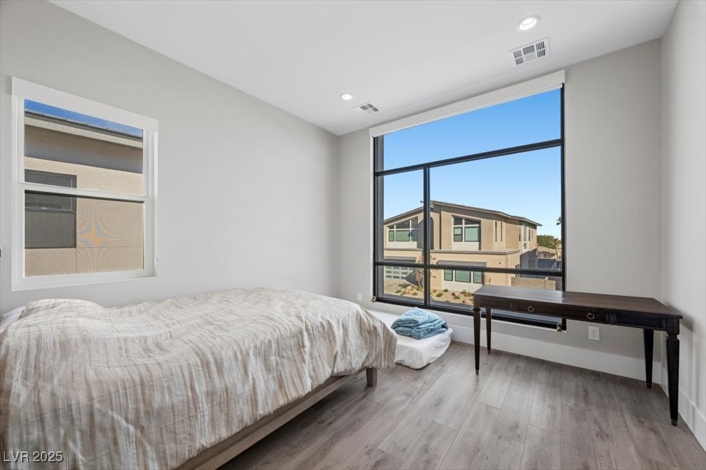 Bedroom with a large black-framed window overlooking neighboring homes and a dark desk.