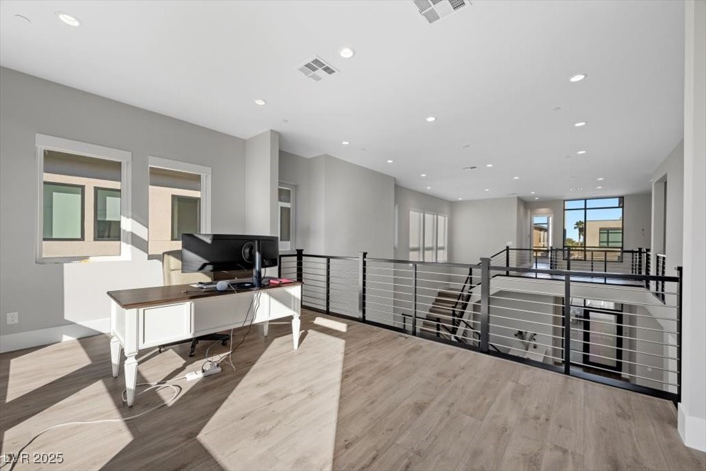 Upstairs loft with a desk beside a black metal railing overlooking the staircase.